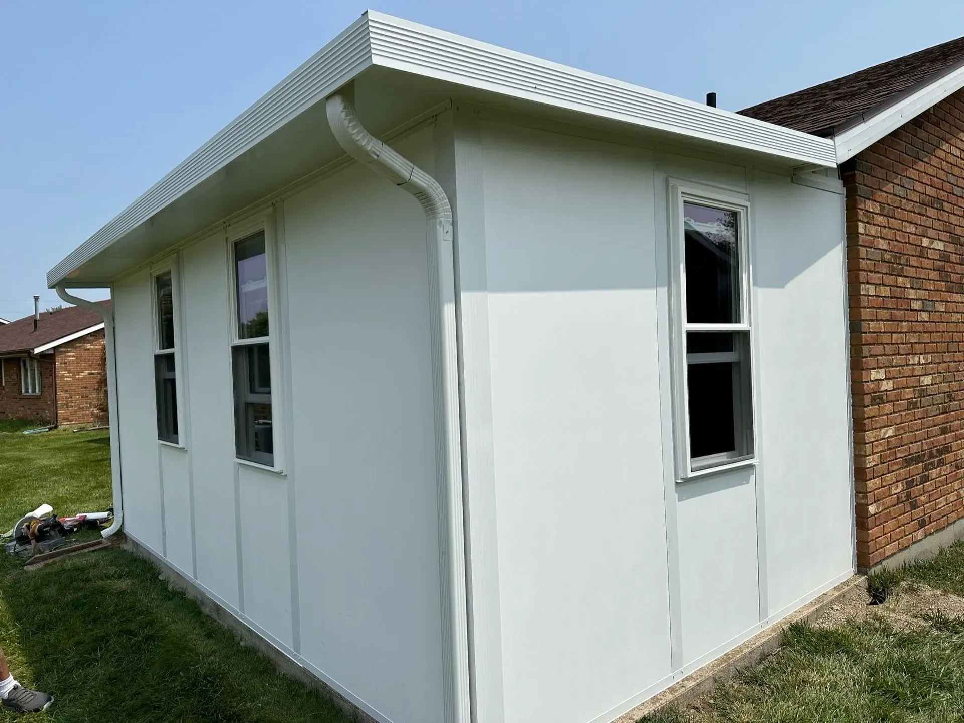 White building addition with windows, white trim, and a brick wall. Sunny outdoor setting.