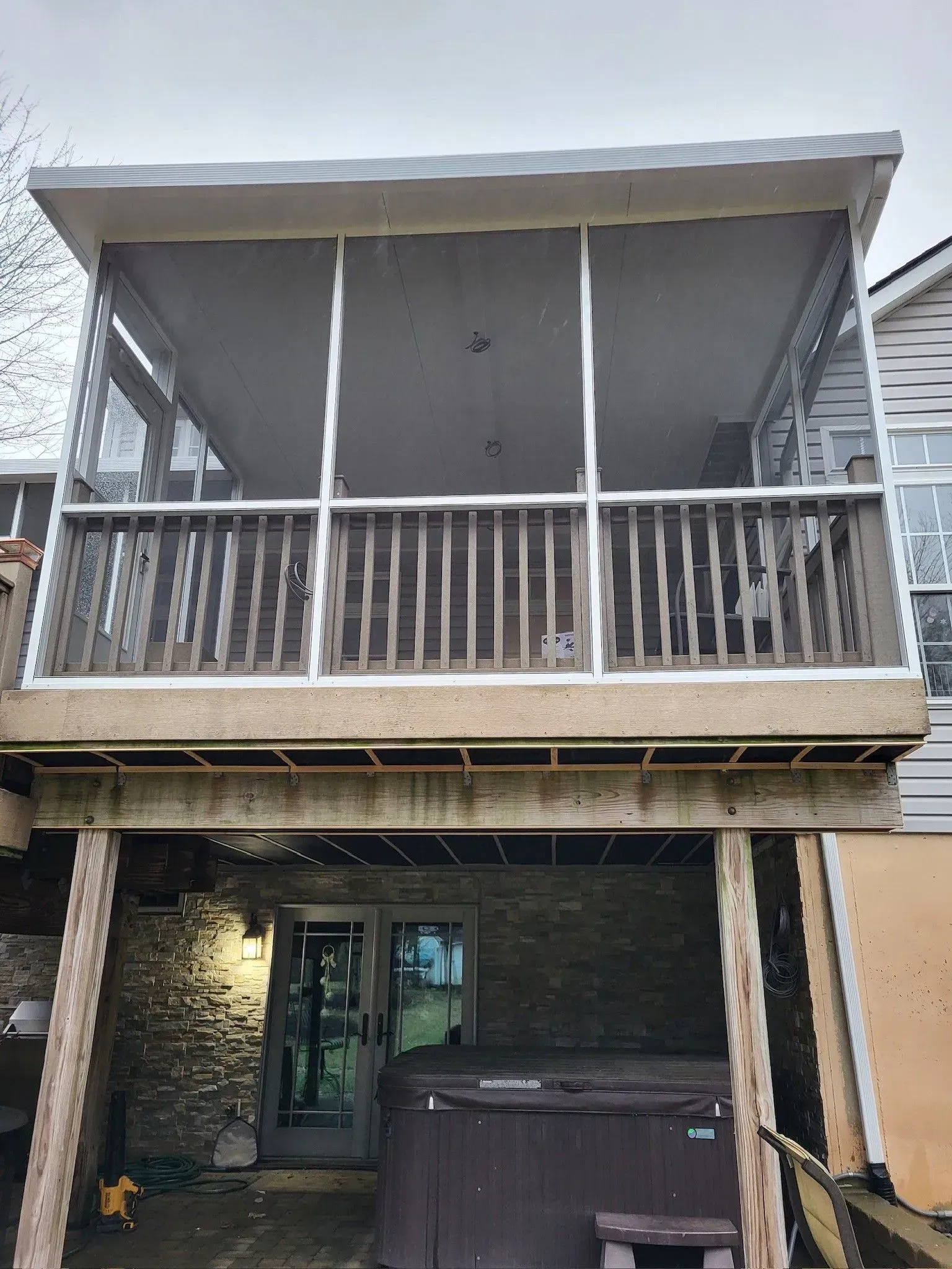 Screened porch with railing over a covered patio; hot tub and door visible below.