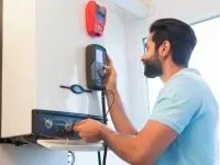Man adjusts control panel on a wall-mounted heating unit, with a red device above.