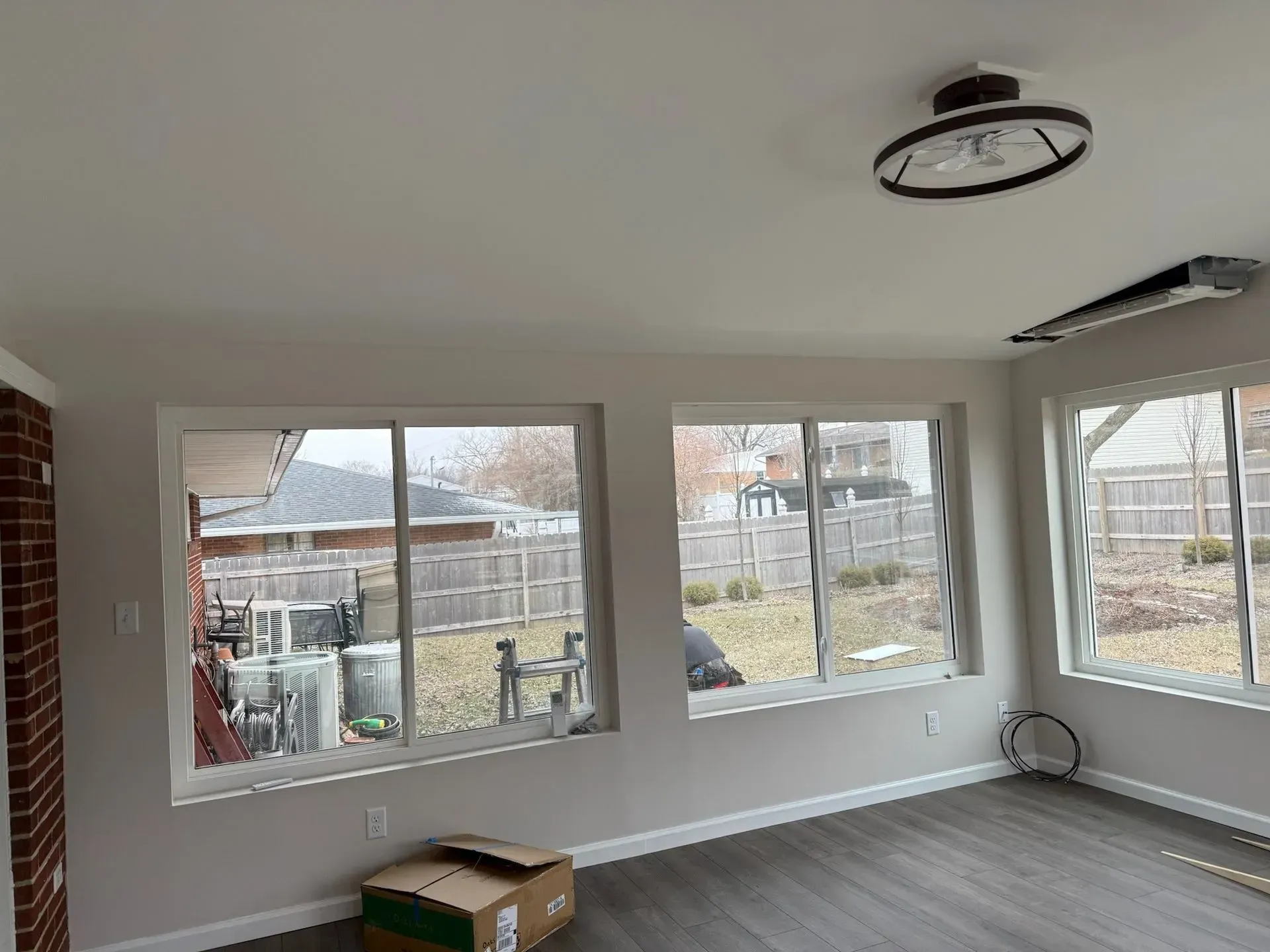 Sunroom interior with windows overlooking a backyard, gray flooring, neutral walls, ceiling light.