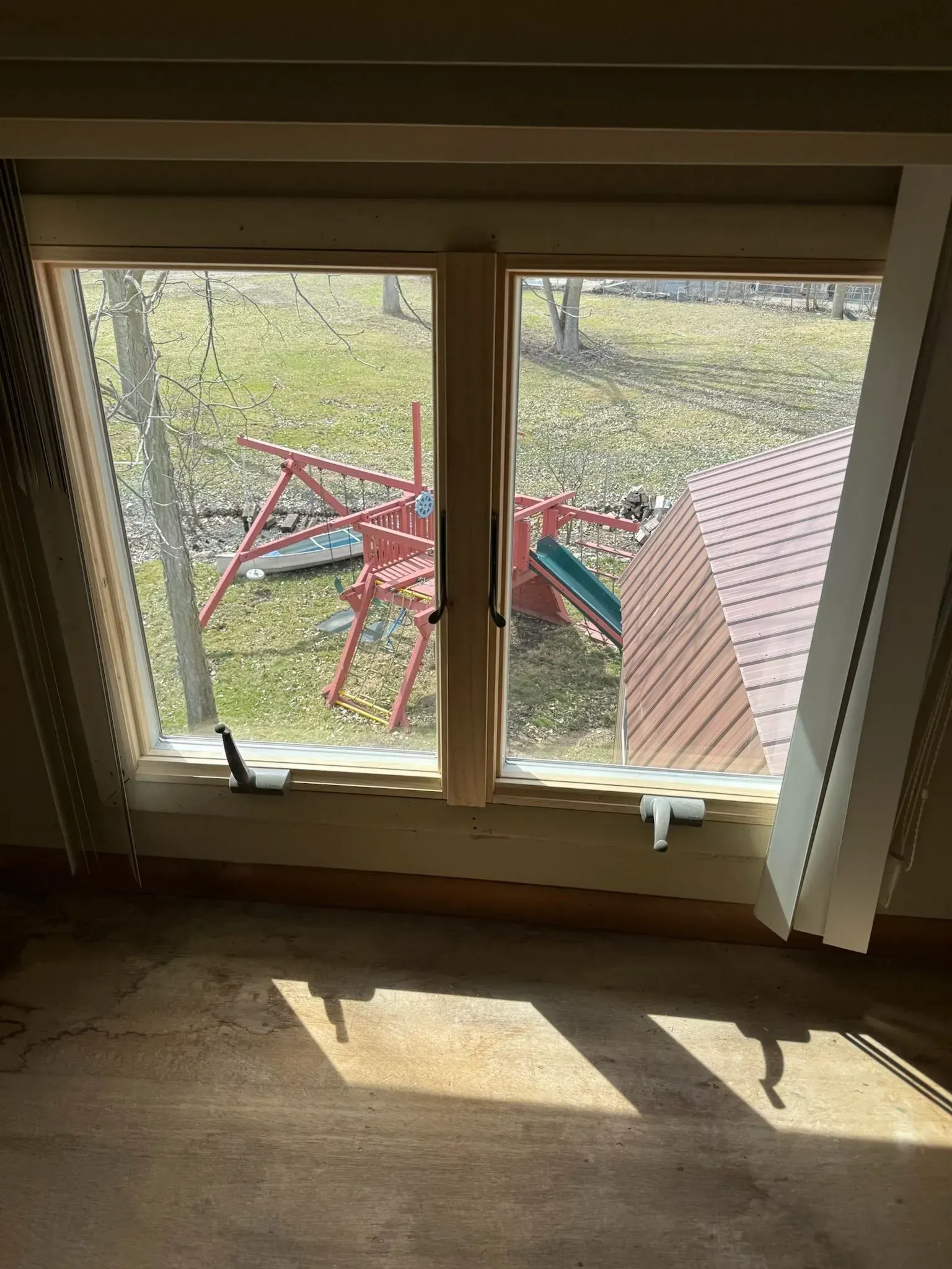 Window overlooking a yard with a red swing set and fall foliage. Sunlight streams into a room.
