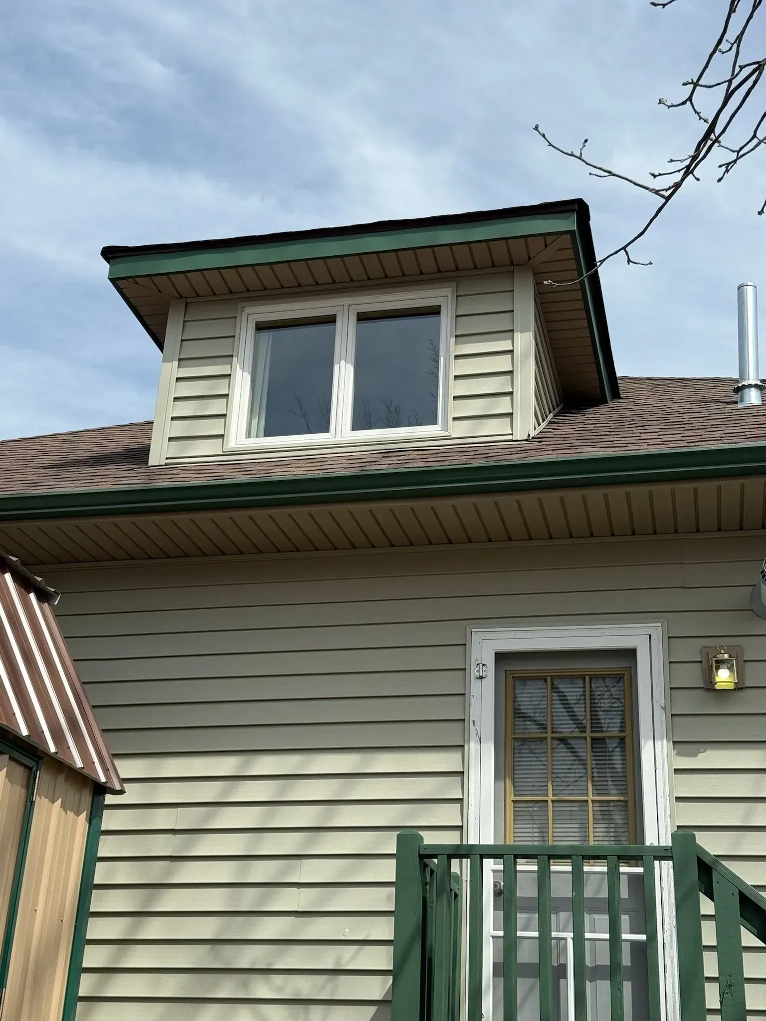 Building exterior with dormer window, green siding, and a small porch with a door.
