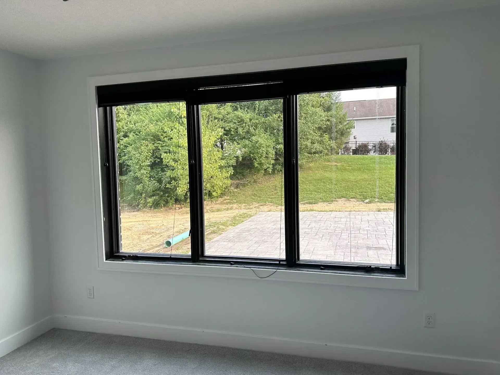 A room with a large window. The window has black trim and looks out onto greenery.