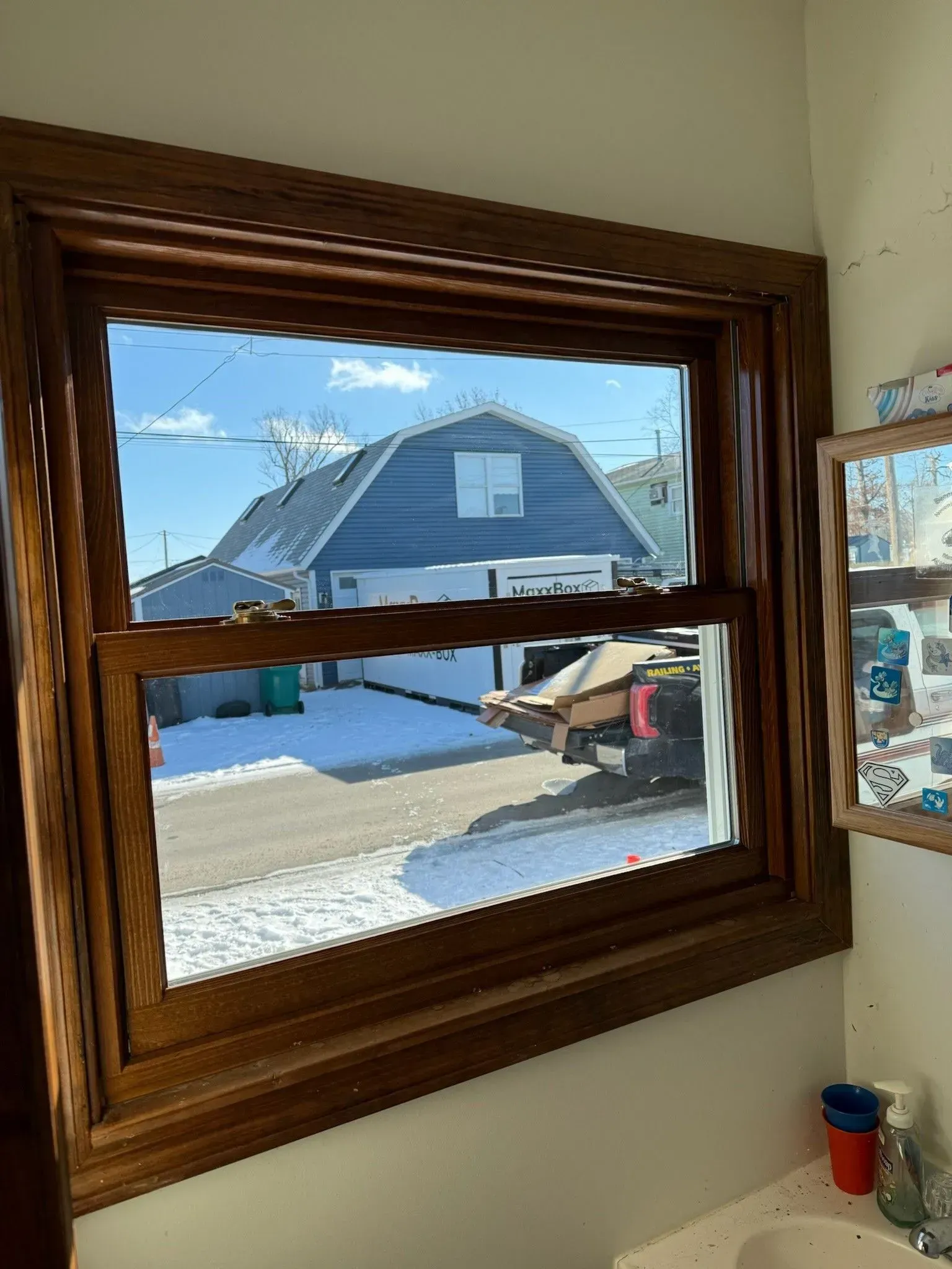 Window with brown wooden frame looking out onto a snow-covered scene with a blue barn.
