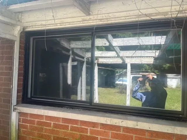 Black-framed sliding window set in a brick wall. A person is reflected in the glass.