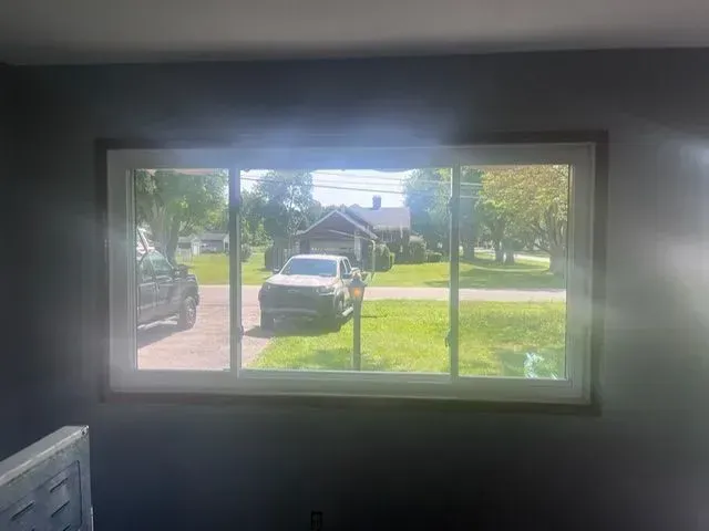 A window looking out onto a residential street with parked cars and a house. Light streams in.