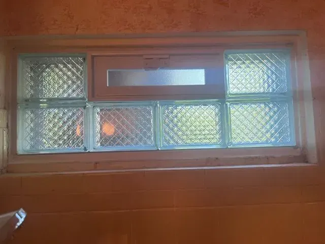 Glass block bathroom window with wooden frame and orange wall.