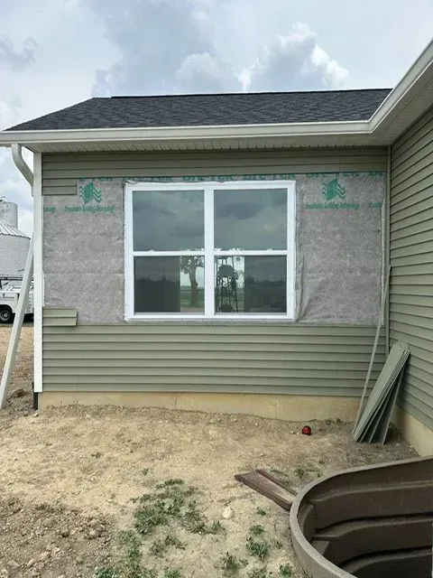 Exterior of a house with a window, partially covered in green siding and weather barrier.