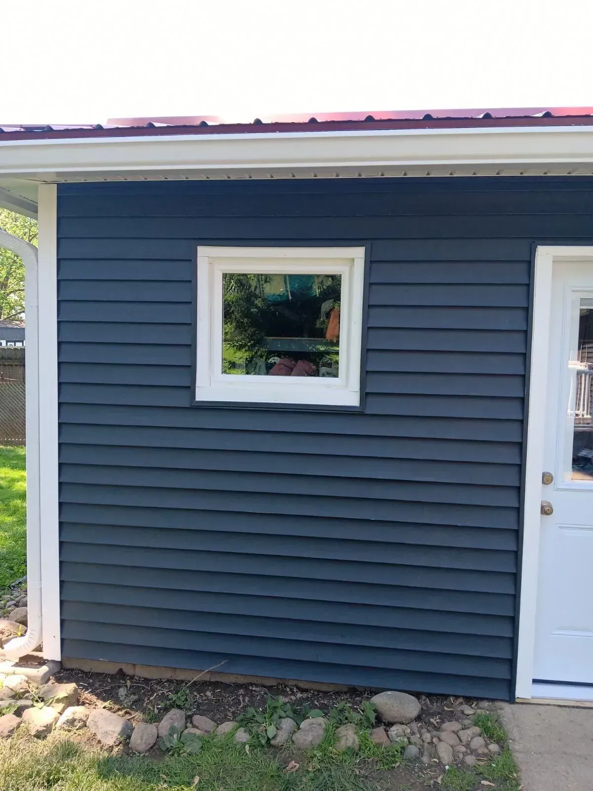 Blue clapboard siding on a building with a white window and trim. Red roof.