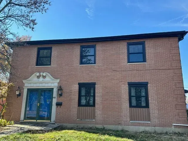 Two-story brick building with black-framed windows, blue front doors, and light-colored trim under a blue sky.