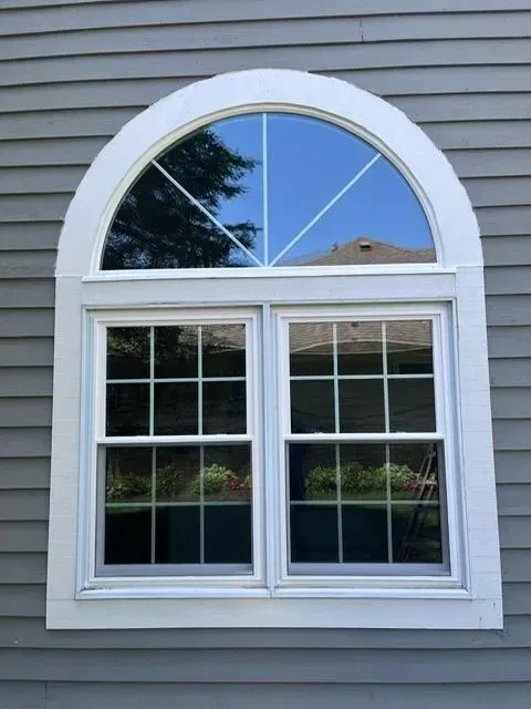 Arched window on a gray house; two lower panes with multiple grids, curved top pane; white trim.