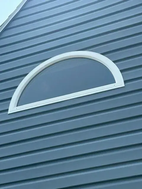 White-framed arched window set in blue horizontal siding on a building's exterior.