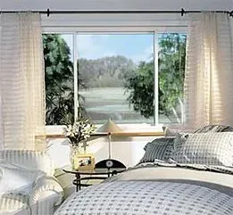 Bedroom with sheer white curtains, large window, bed, and decorative lamp.