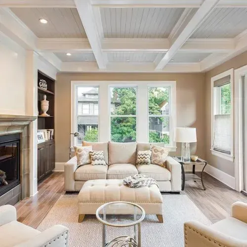 Living room with beige walls, cream sofa, ottoman, and white ceiling beams.