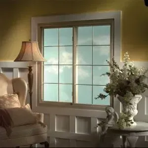 Cozy living room with window overlooking sky, armchair, lamp, flowers in a vase, and side table.