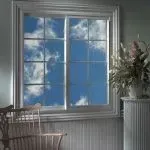 Window with a bright blue sky and clouds; a wooden chair and a flower arrangement are beside the window.