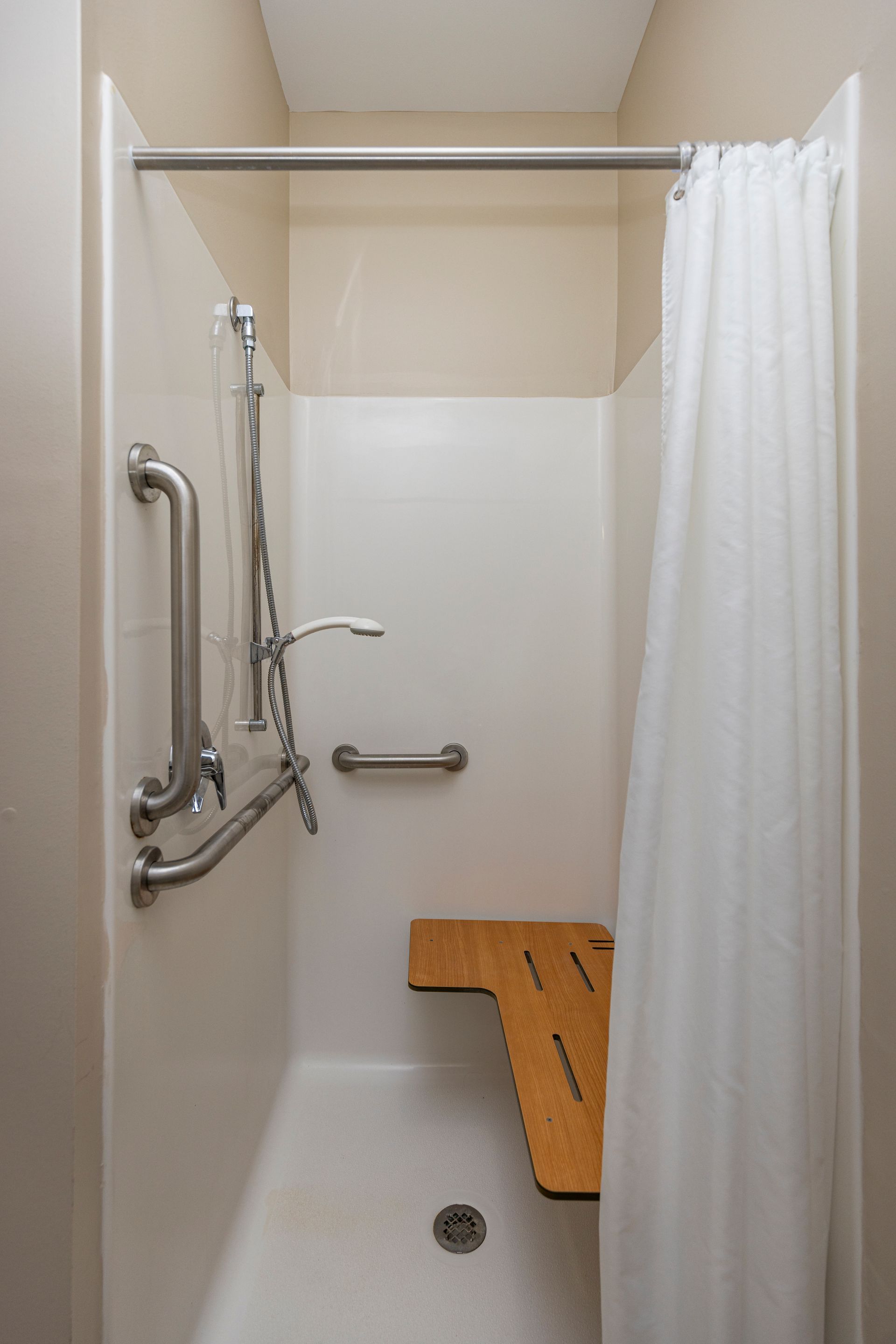 An accessible walk-in shower with a wooden bench, multiple grab bars, and a handheld showerhead.