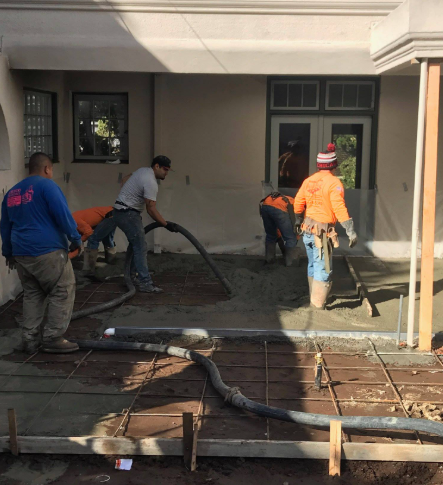 Construction workers pouring concrete on a patio with rebar framework.
