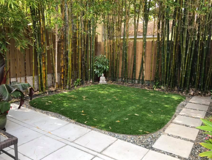 A zen garden with bamboo, artificial grass, stone path, and a Buddha statue.