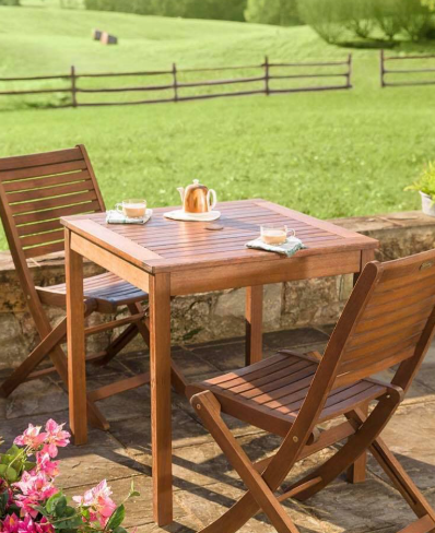 Wooden table and chairs set up outdoors with tea service. Rolling green landscape in the background.
