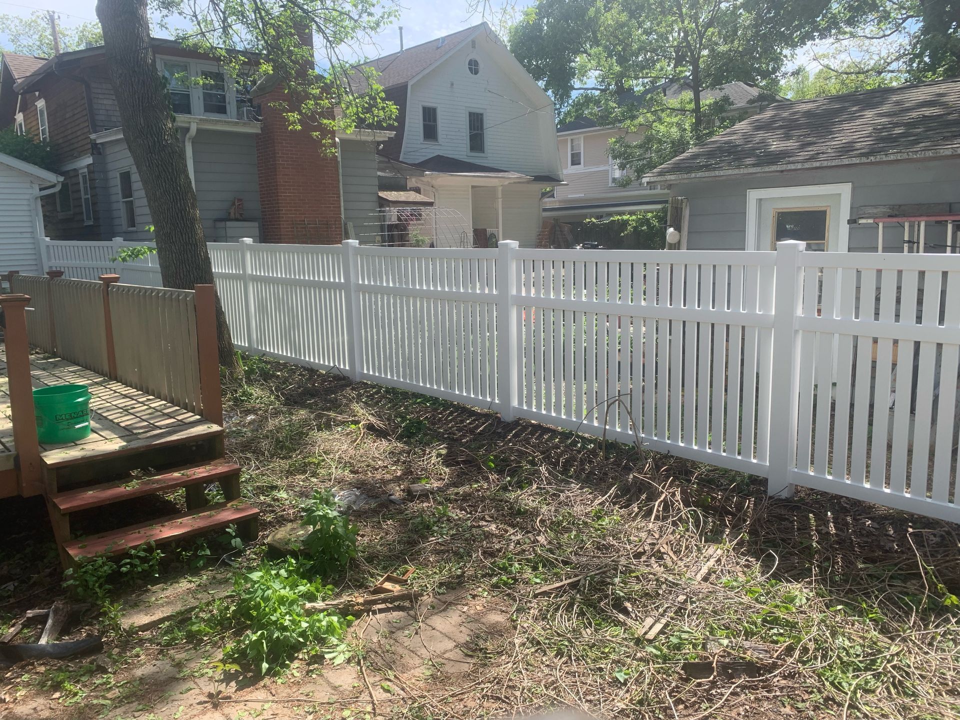 A white fence surrounds a large house with a pool in the backyard.