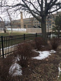 A fence with a tree in the background and a building in the background.