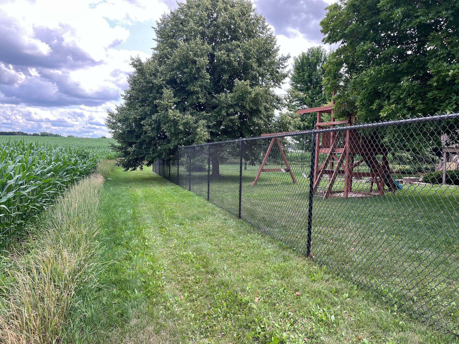 A chain link fence surrounds a playground in a field.
