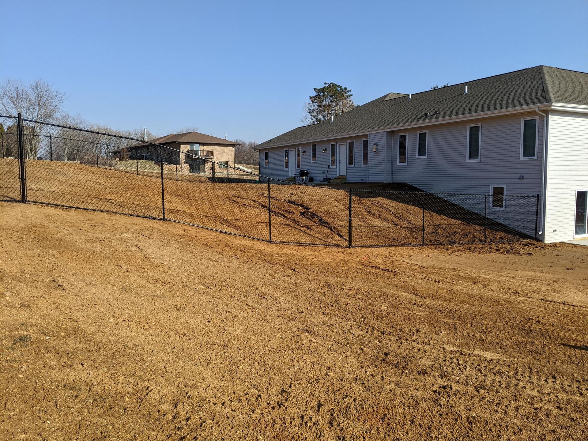 A house is sitting on top of a dirt hill next to a fence.