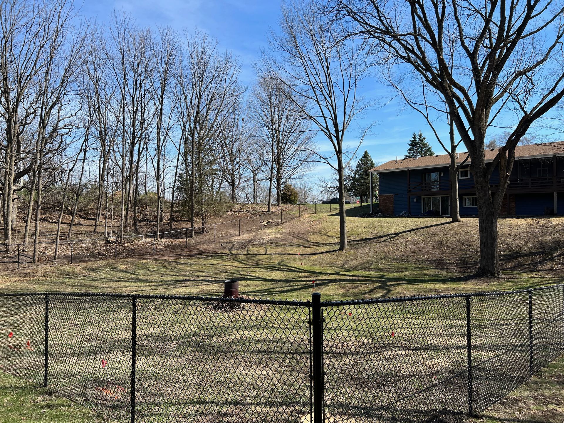 A chain link fence surrounds a grassy field with trees in the background.