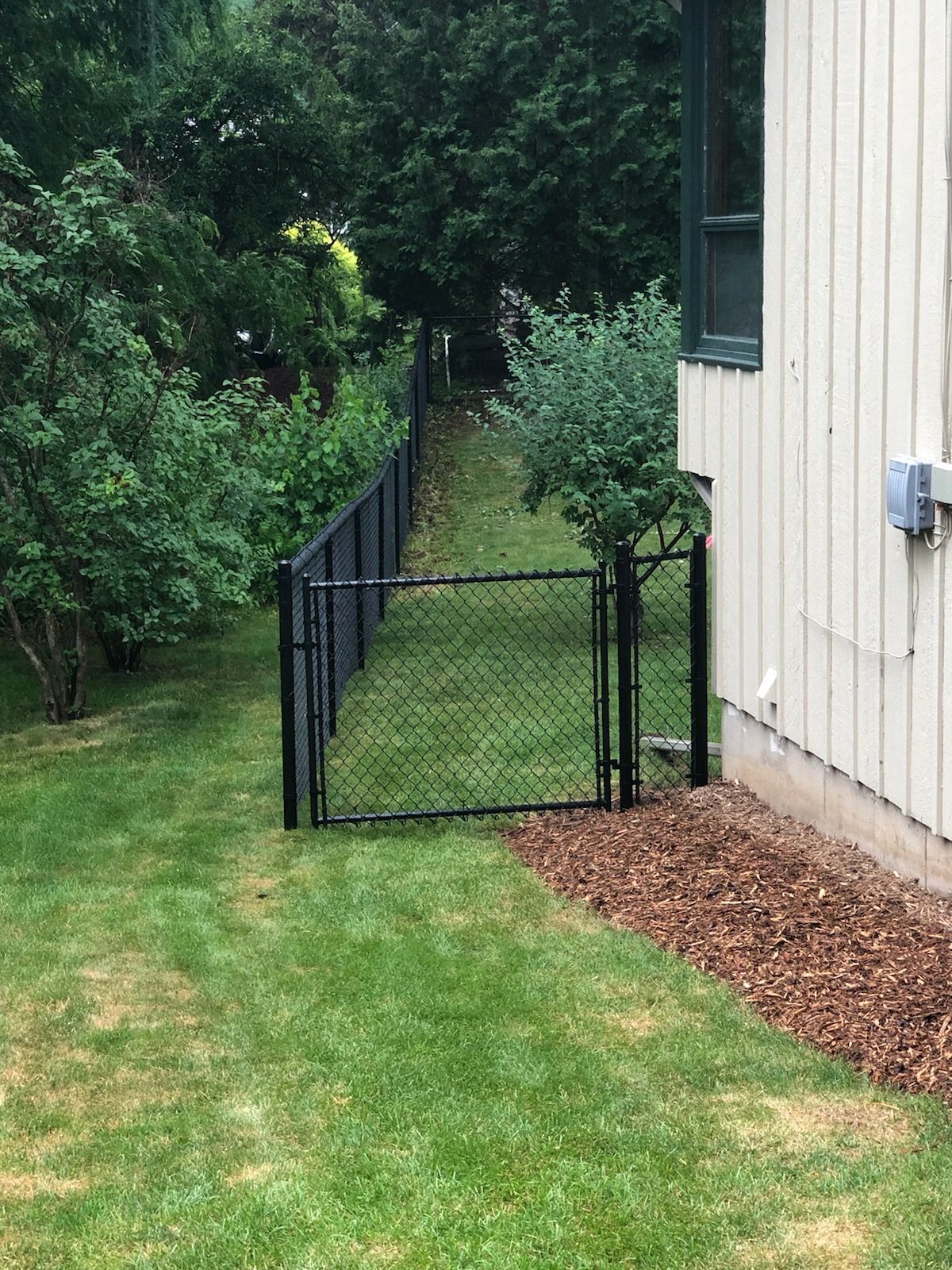 A chain link fence with a gate in the backyard of a house.