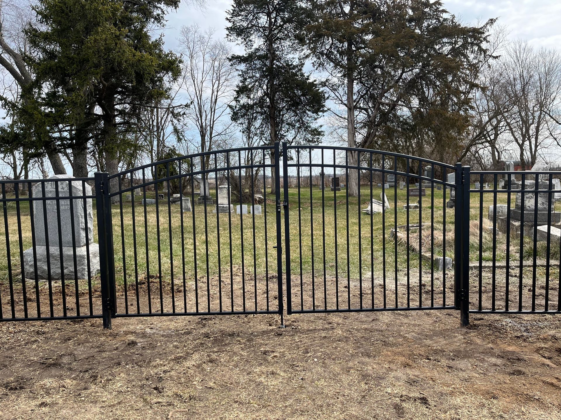 A wrought iron gate is surrounding a cemetery with trees in the background.