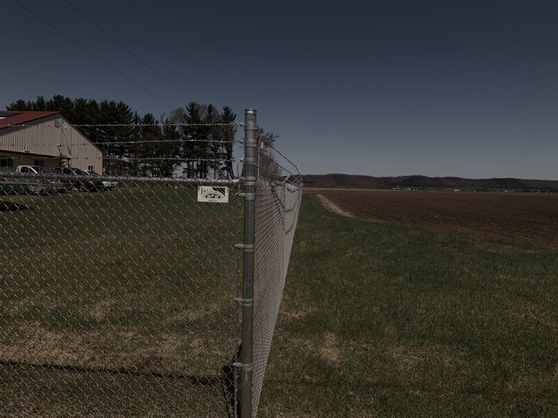 A chain link fence surrounds a field with a building in the background