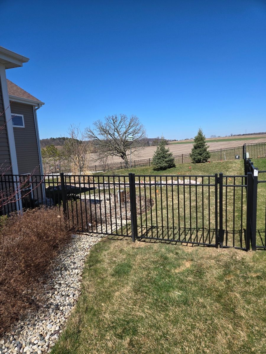 A black fence surrounds a lush green yard in front of a house.