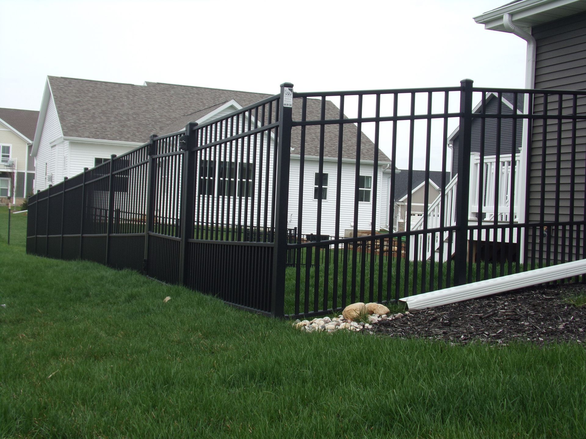 A black fence surrounds a lush green yard in front of a house