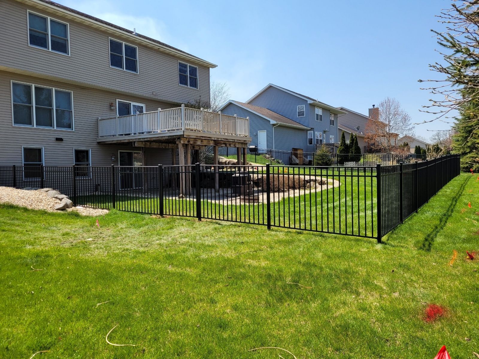 A black fence surrounds a lush green yard in front of a house.