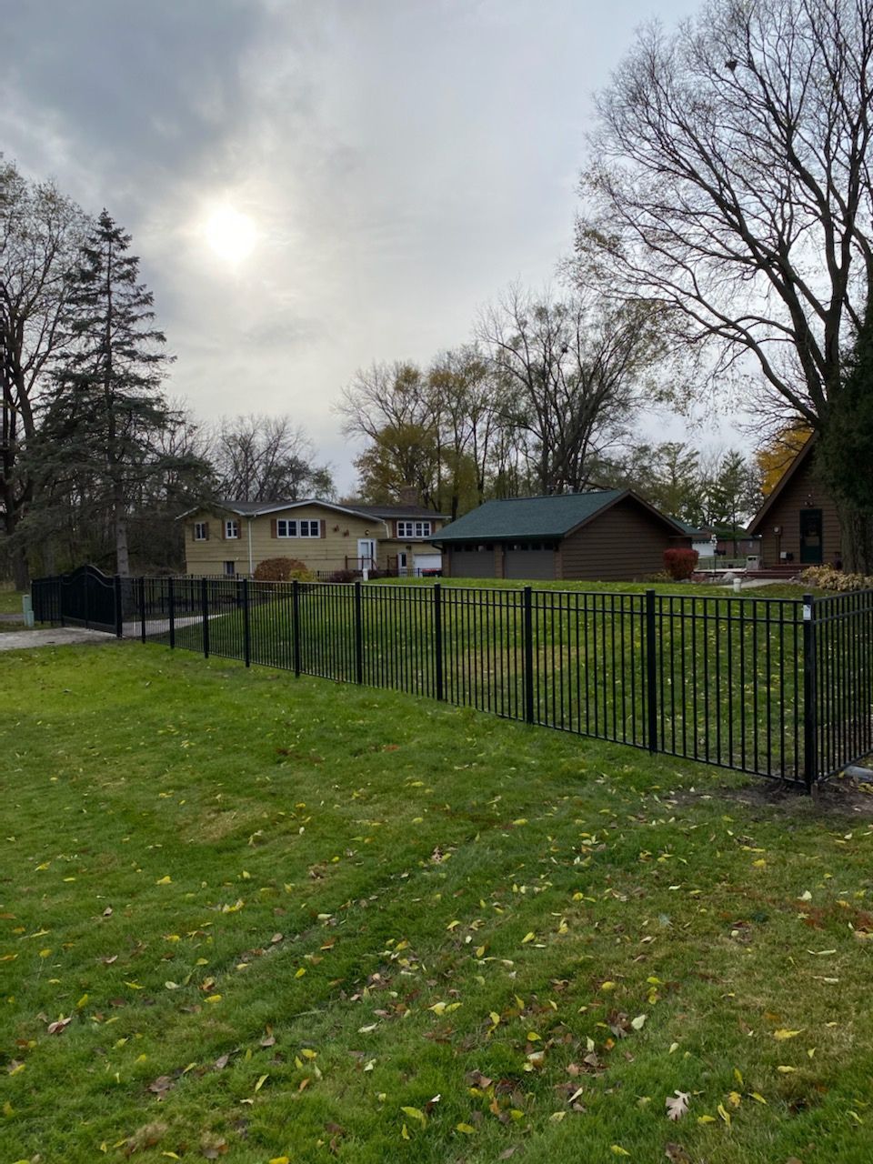 A fence surrounds a lush green field with a house in the background.