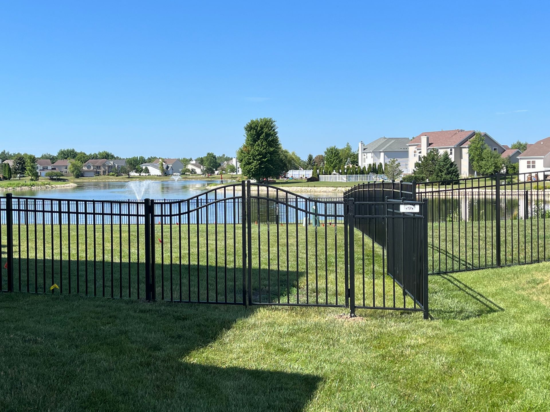 A black fence surrounds a lush green field with a lake in the background.