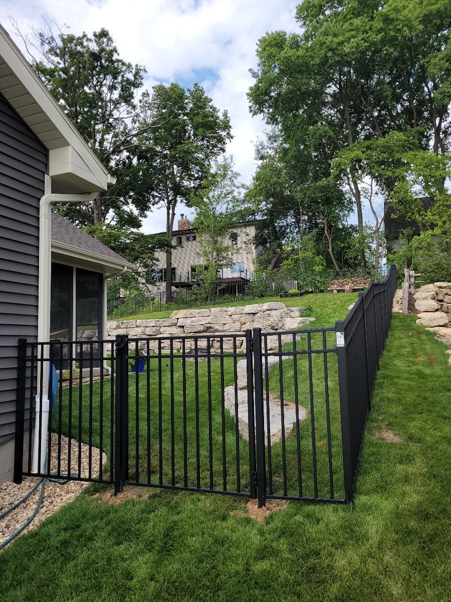 A black fence surrounds a lush green yard in front of a house.