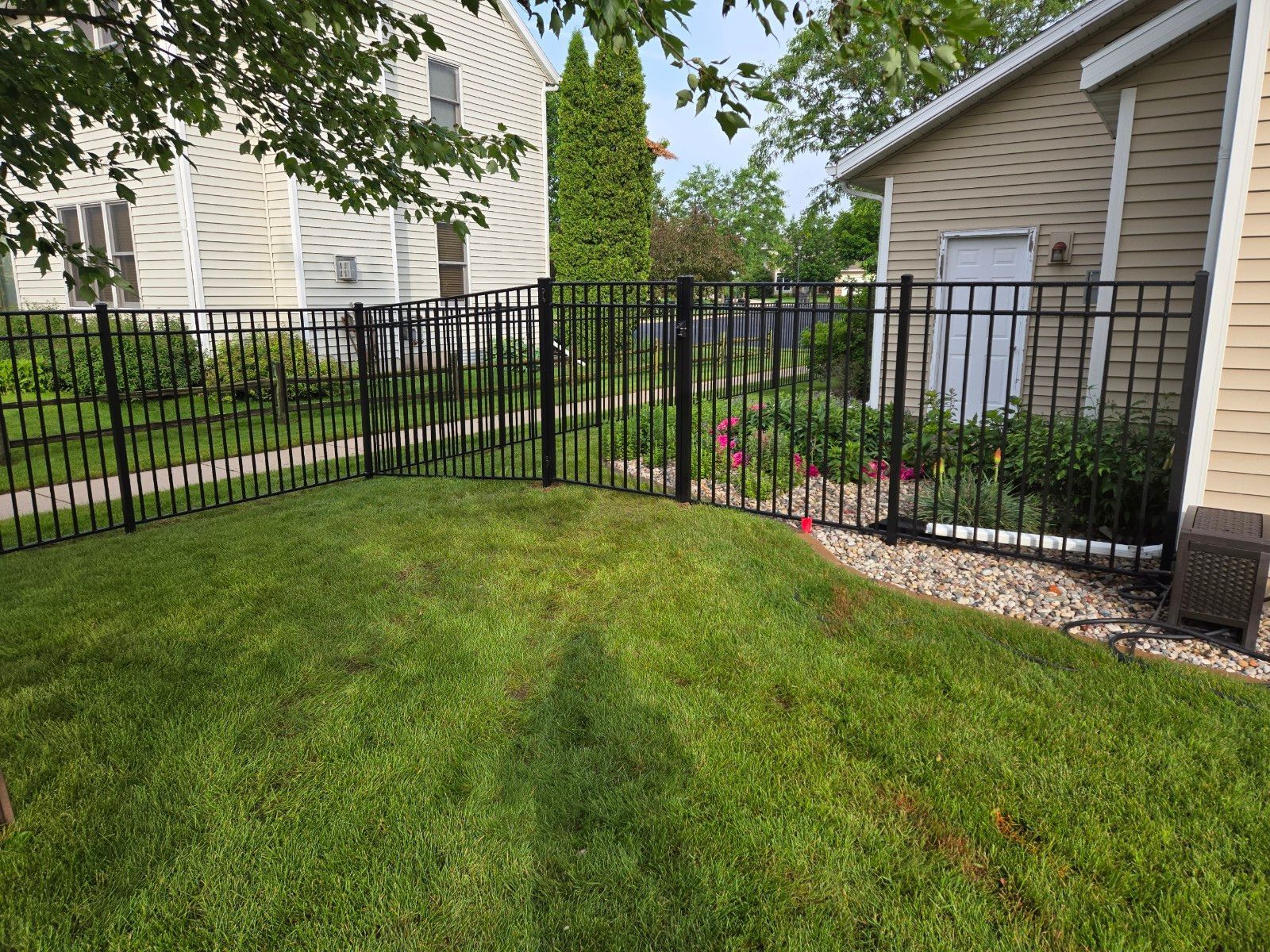 A black fence surrounds a lush green yard in front of a house.