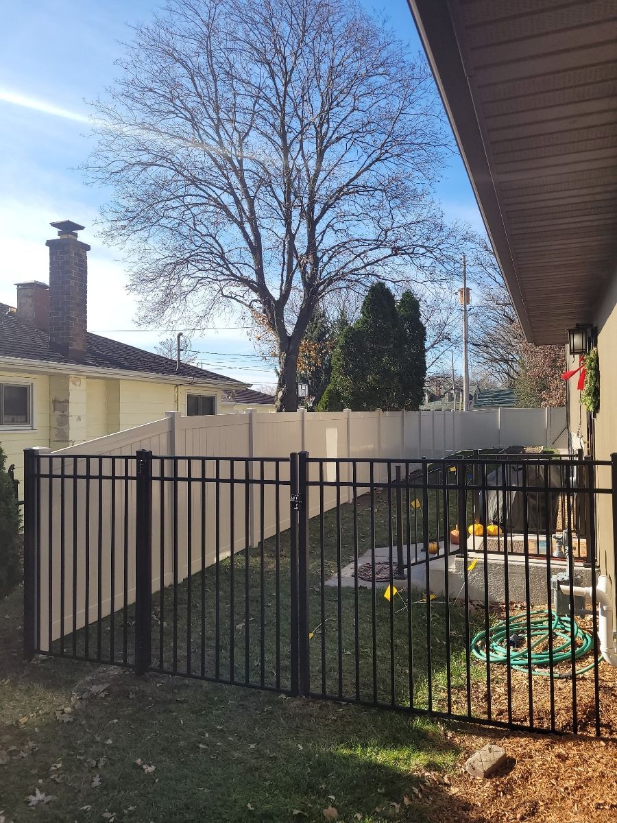 A black fence surrounds a backyard with a white fence and a tree in the background.