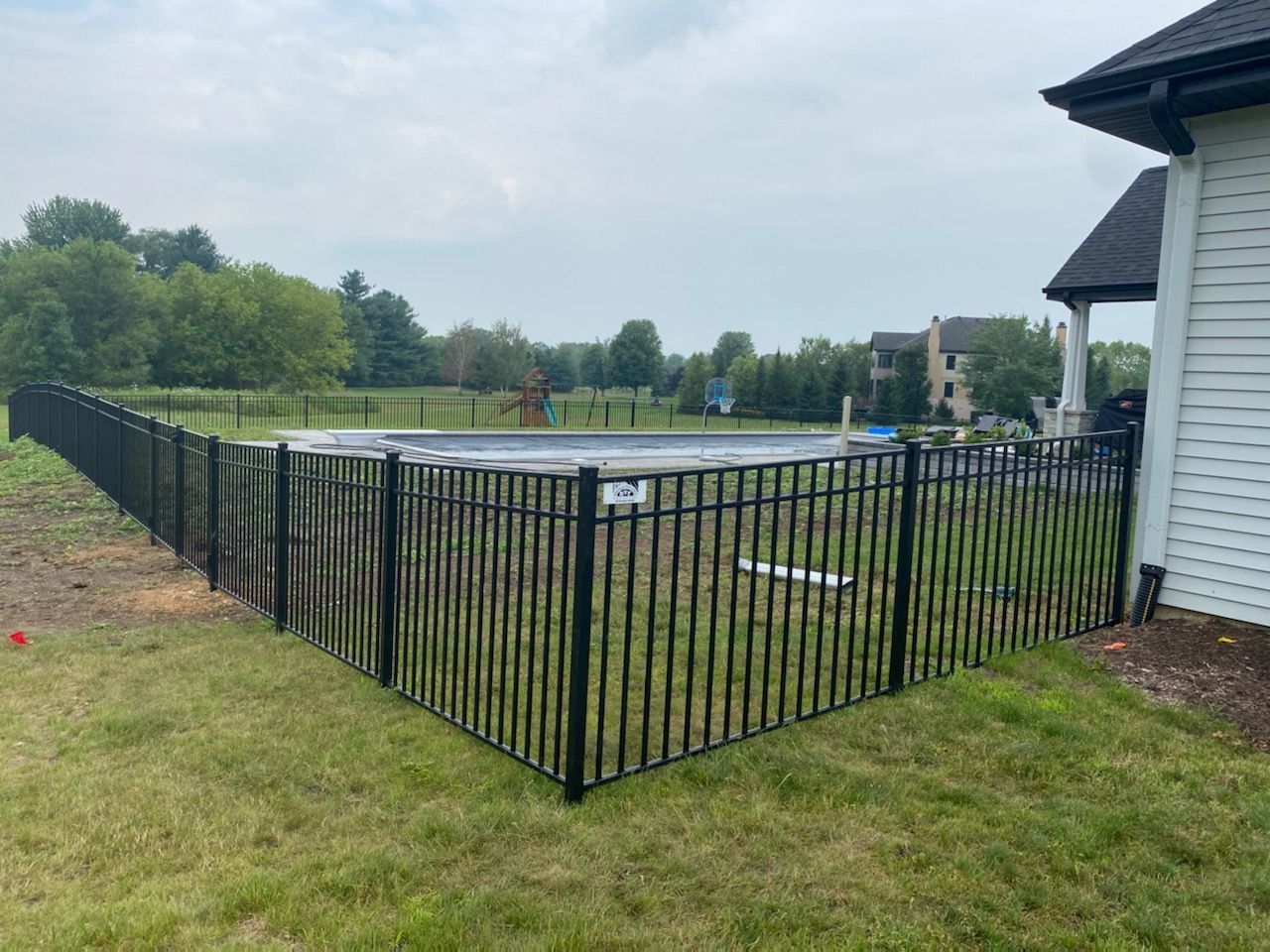 A black metal fence surrounds a swimming pool in a backyard.