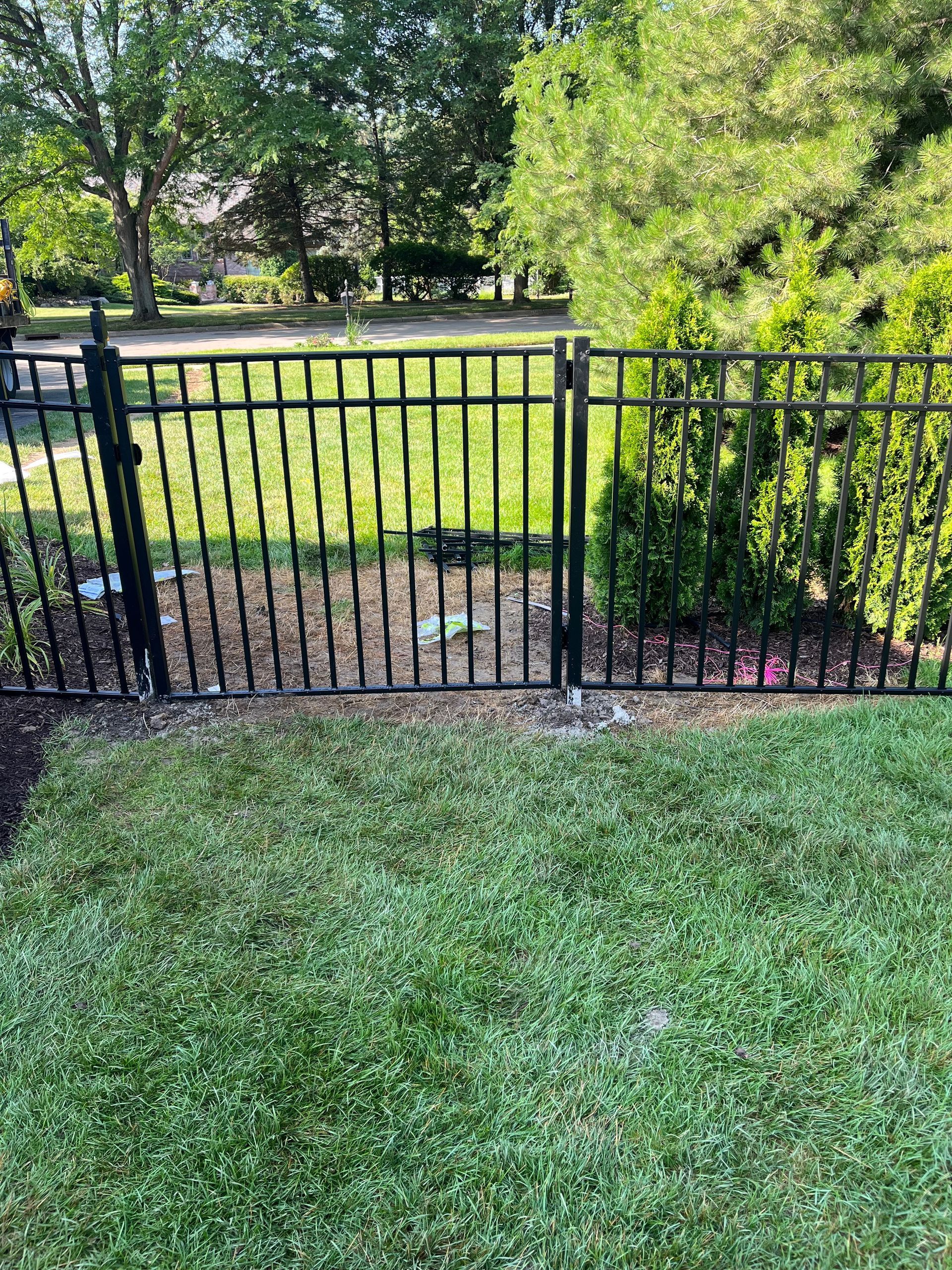 A black metal fence is surrounded by lush green grass and trees.