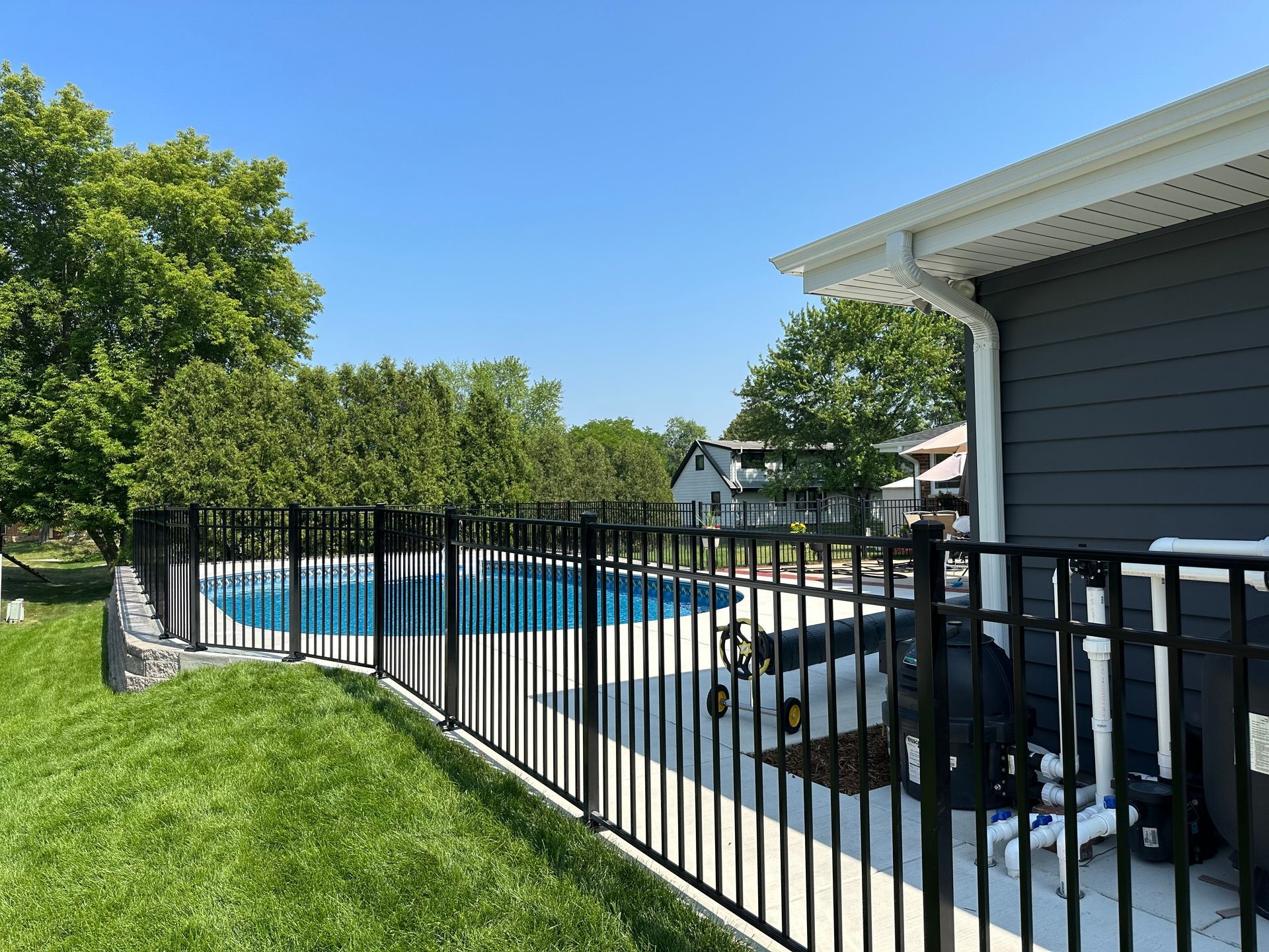 A black fence surrounds a swimming pool in a backyard.