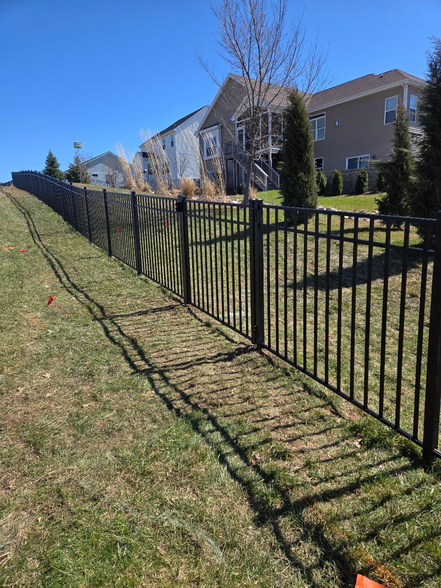 A black metal fence surrounds a grassy yard in front of a house.