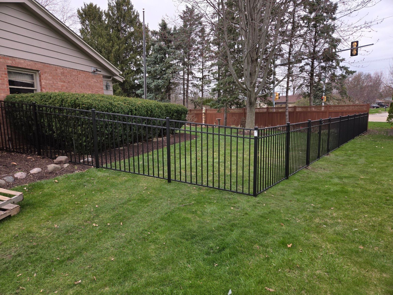 A black metal fence surrounds a lush green yard in front of a brick house.