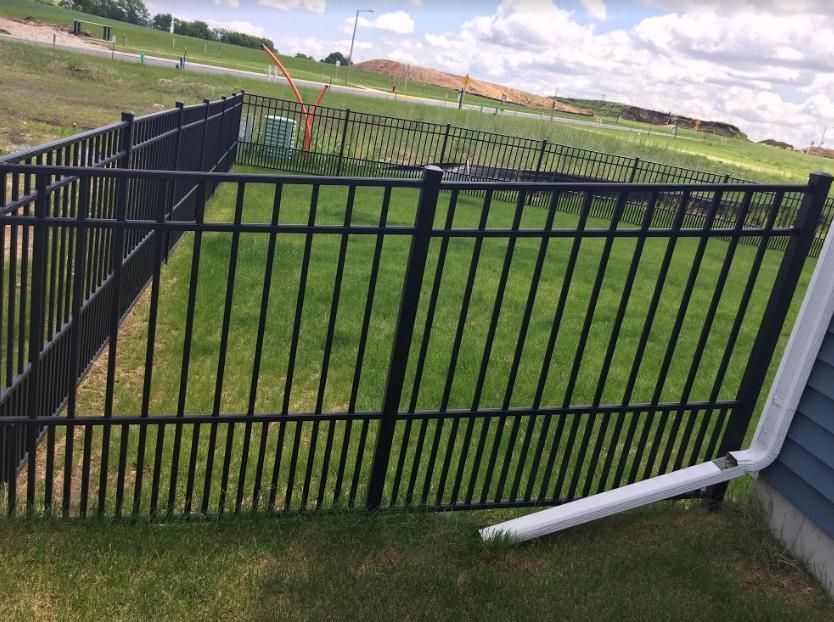 A driveway with a fence and a house in the background