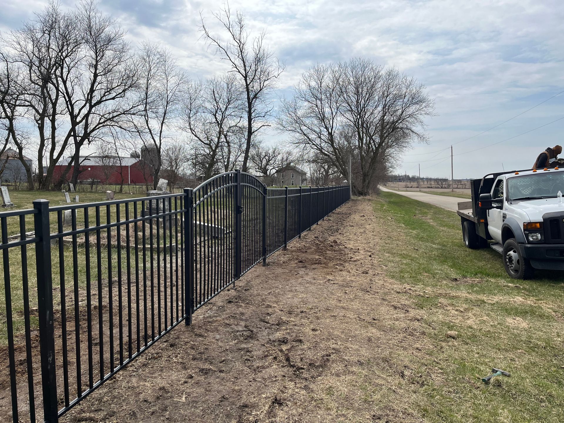 A white truck is parked next to a black fence in front of a cemetery.