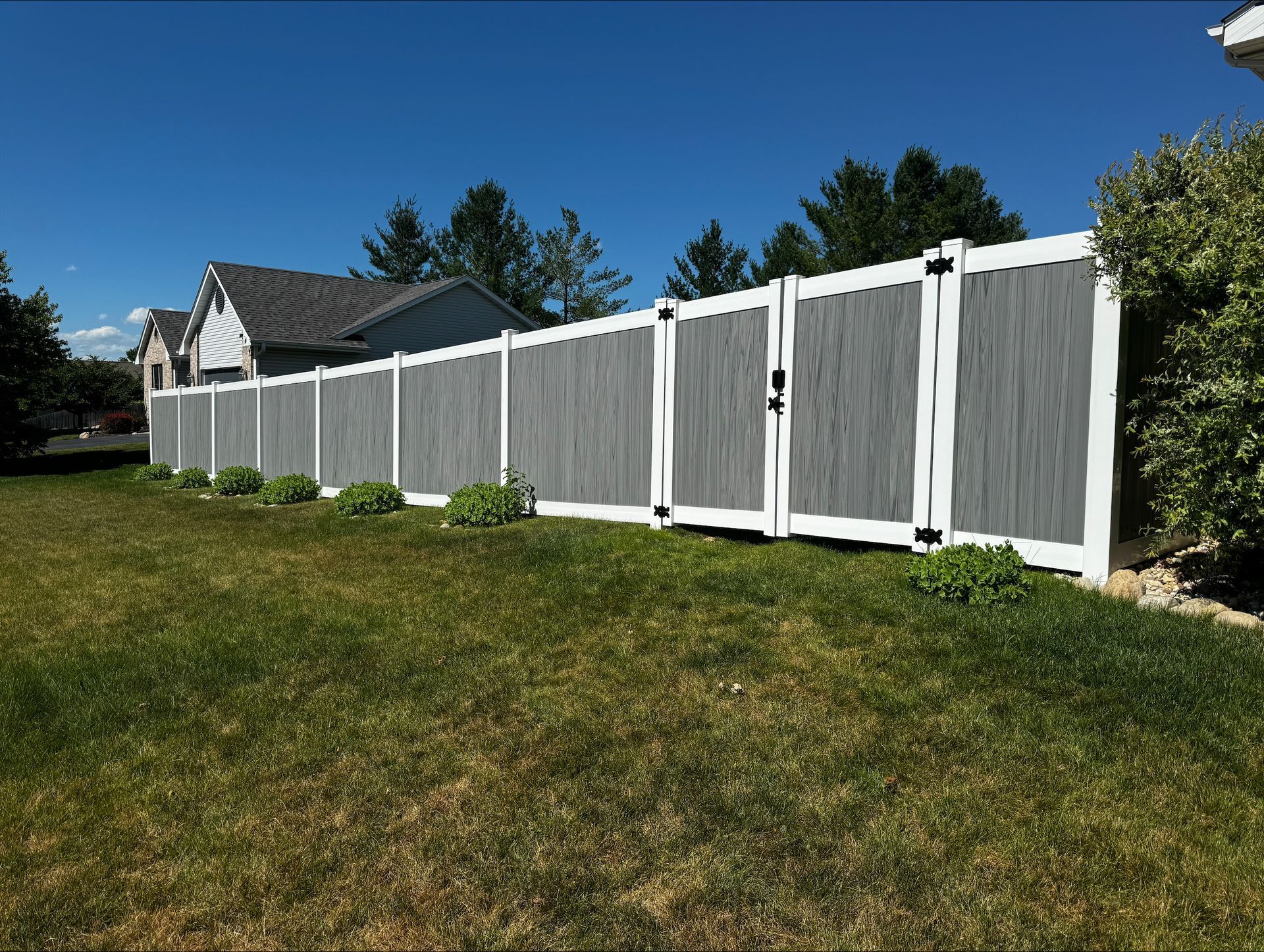 A white and gray fence surrounds a grassy yard in front of a house.