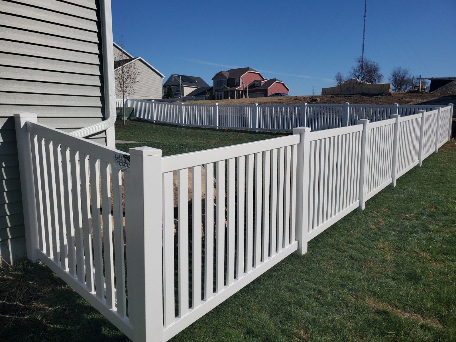 A white fence surrounds a lush green yard in front of a house.