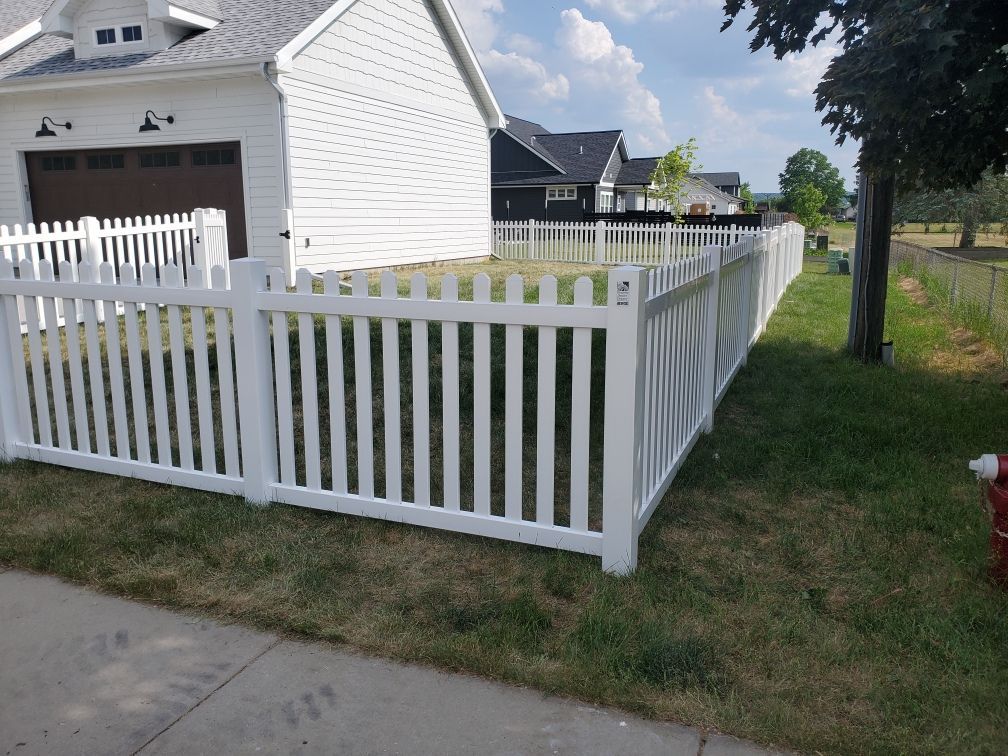 A white picket fence surrounds a yard in front of a house.